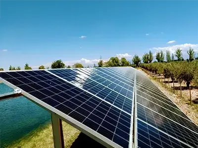 Paneles solares instalados en campo agrícola junto a canal de riego y árboles